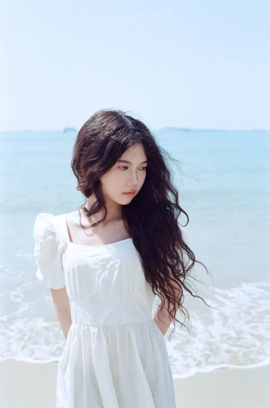 一位穿着白色连衣裙的美女站在海滩上 背景是海洋。