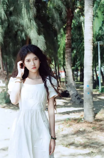 一位穿着长白色连衣裙的年轻女子在棕榈树前摆姿势