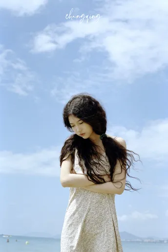 一位穿着白色连衣裙的年轻女子站在海滩上 眺望着蓝色的海洋。