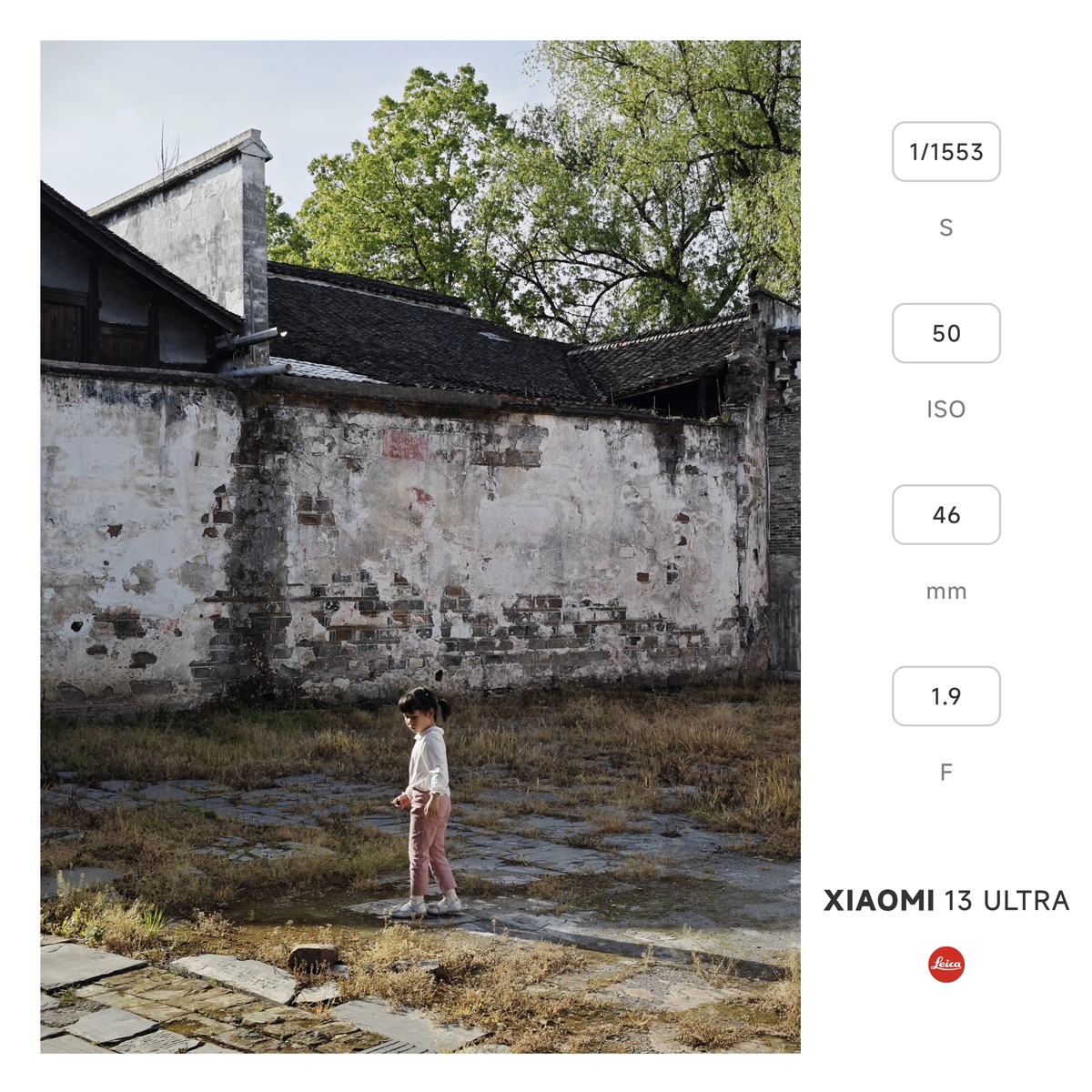 一个小女孩站在一个水坑旁边 旁边有一堵墙 墙里面有人玩。