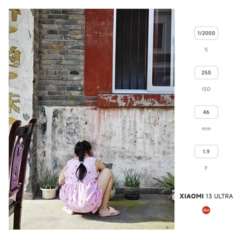 一个小女孩穿着粉红色裙子坐在一家破败房屋的门口 这家房屋旁边有一座破败的建筑。