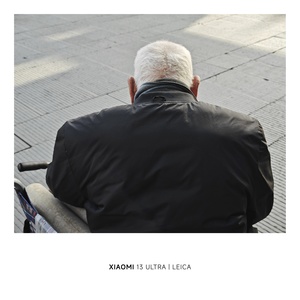 一个老人穿着一件皮夹克坐在长凳上
