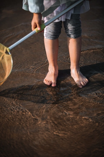 一个年轻女孩拿着网球拍站在地板上 双脚在水里 后面有人拿着网。