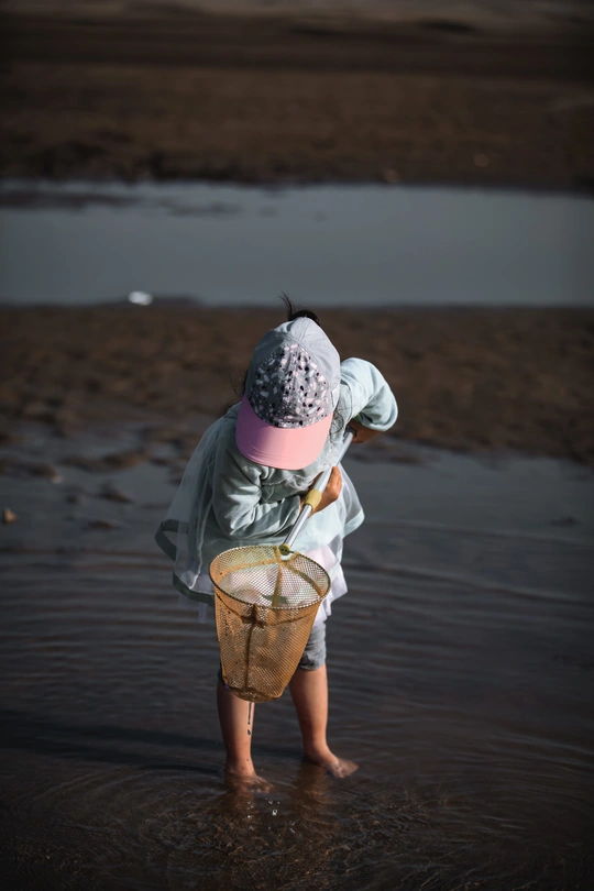 一个小女孩站在海滩上 在一个小碗里玩水。
