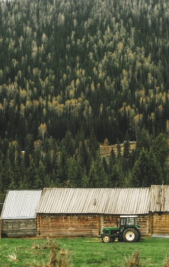 一个小卡车停在一片绿草地上 前面有一座木制的谷仓 背景中有树木和山脉。