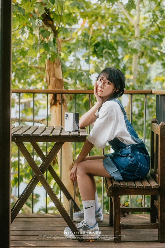 一个戴着眼镜的年轻女子坐在甲板上的木长椅上