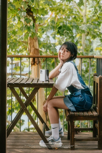 一个戴着眼镜的年轻女子坐在甲板上的木长椅上