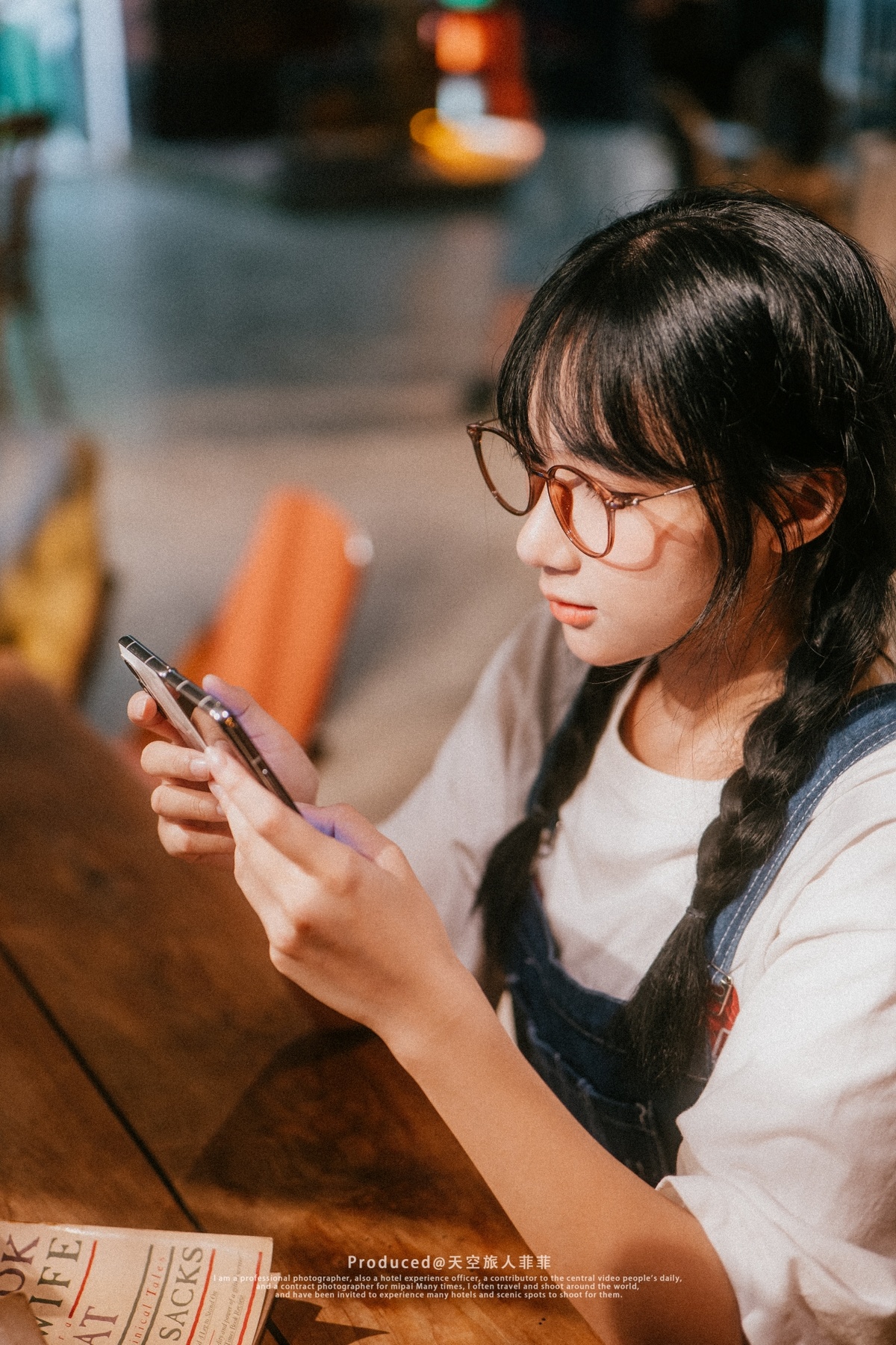 一位戴着眼镜的年轻女子坐在木桌旁看手机