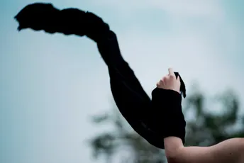 一位女士举着一把黑色雨伞在头上 天空中一只风筝在飞翔。