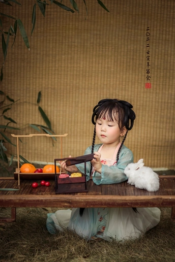 一个穿着连衣裙的年轻女孩抱着一只小白兔坐在桌子前的木长椅上