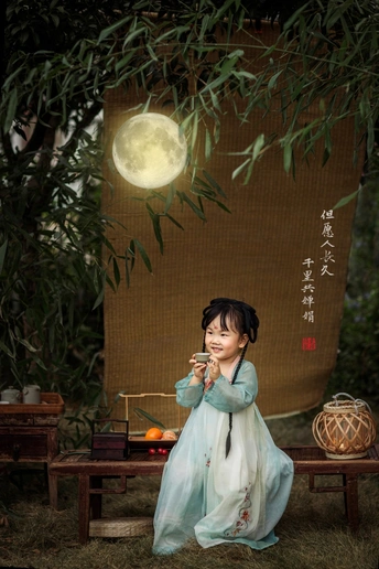 一个穿着中国传统服饰的小女孩坐在满月下
