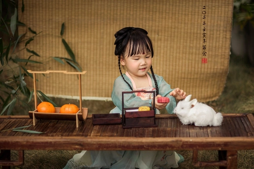 一个小女孩坐在木桌旁玩一只白兔和一盒桔子