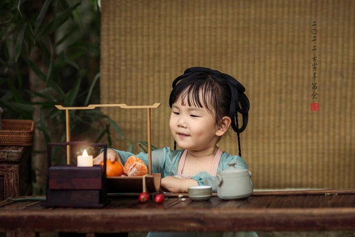 一个小女孩坐在桌子旁 手里拿着一杯茶和一个小娃娃