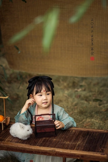 一个拿着相机的年轻女孩坐在木长椅上 桌子上的盒子里放着一个小毛绒玩具