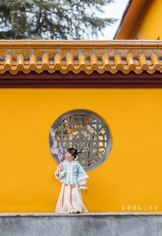 一位穿着传统服装的年轻女孩站在黄色墙壁前