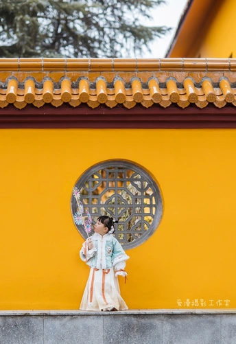 一位穿着传统服装的年轻女孩站在黄色墙壁前