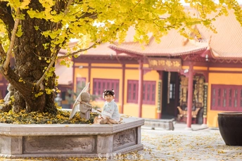 一个小男孩和一个小女孩坐在寺庙前面的一棵树下。