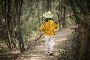 一个戴黄帽的小女孩走在森林小径上拿着一根棍子