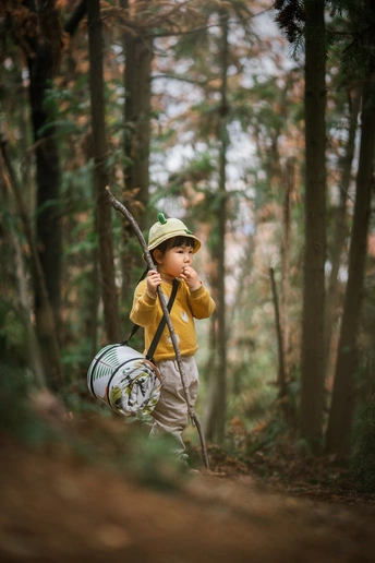 一个戴帽子背书包的男孩拿着棍子在森林里穿过树林