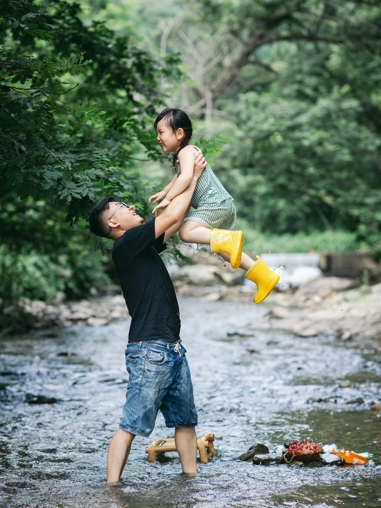 一个抱着年轻男孩在河或小溪中玩耍的男子 同时婴儿在水中玩耍。