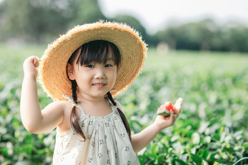 一个小女孩戴着草帽 手里拿着一个苹果 站在草莓地的草莓植株中间 小女孩正在吃一个苹果。