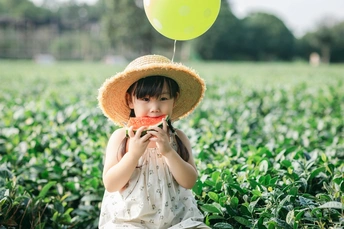 一个戴帽子的小女孩在田地里摘水蜜桃 手里拿着一个气球。