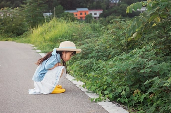 一个戴帽子的年轻女孩坐在路边的滑板上 手里拿着一把黄色雨伞和一个小小的行李箱。