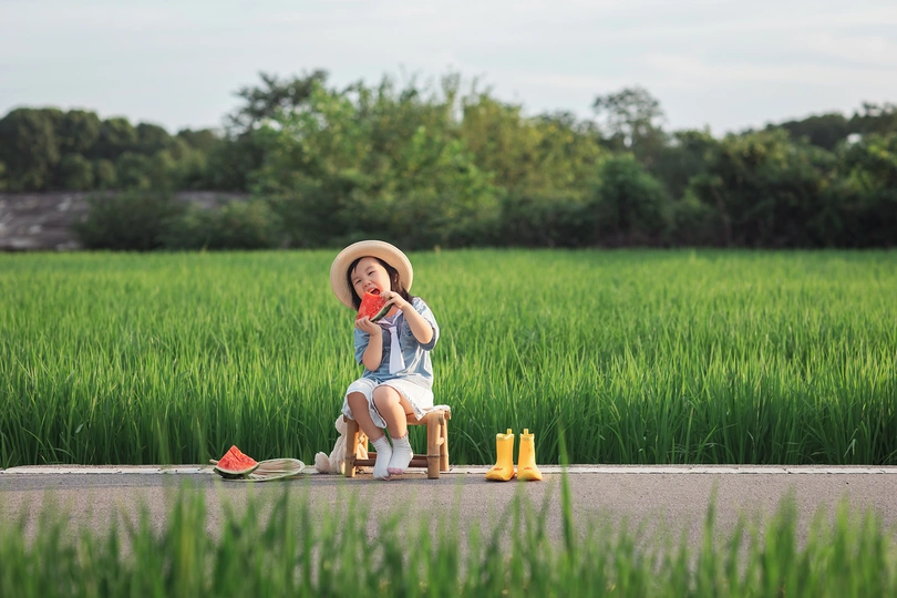 一个戴帽子的小女孩坐在路边 在绿草地上玩她的玩具。