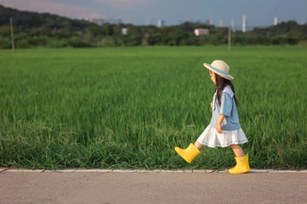 一个穿着连衣裙、帽子、黄色靴子的年轻女孩在绿色的田野中走下道路