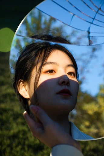 一位年轻女子举着镜子照镜子仰望着天空