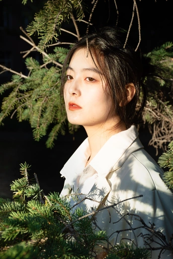 一位穿着白色和服的年轻女子站在松树丛中