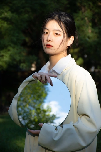 一位穿着全白的年轻女子手里拿着一面镜子