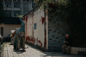 一位老人坐在小巷的人行道上 墙上有一栋血迹斑斑的建筑