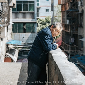 一位老人站在阳台上 眺望着城市街道和建筑物。