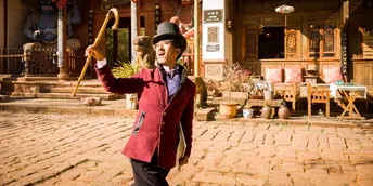 一个穿着红夹克和帽子 拿着棍子走下鹅卵石街道的男人