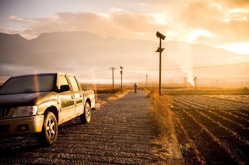 一辆卡车行驶在泥土路上 路边停着一辆汽车 背景是山脉。