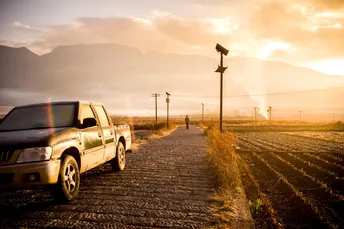 一辆卡车行驶在泥土路上 路边停着一辆汽车 背景是山脉。
