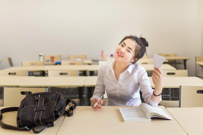 一个年轻女子坐在教室的桌子旁 桌子上堆满了书籍和纸张。