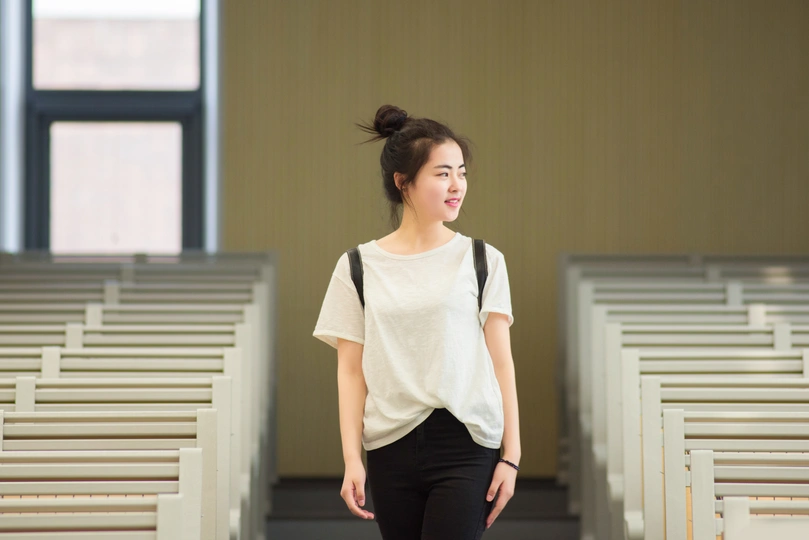 一位穿着白色衬衫和黑色裤子的年轻女子穿过一座空荡荡的教堂。