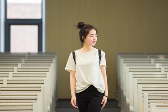 一位穿着白色衬衫和黑色裤子的年轻女子穿过一座空荡荡的教堂。