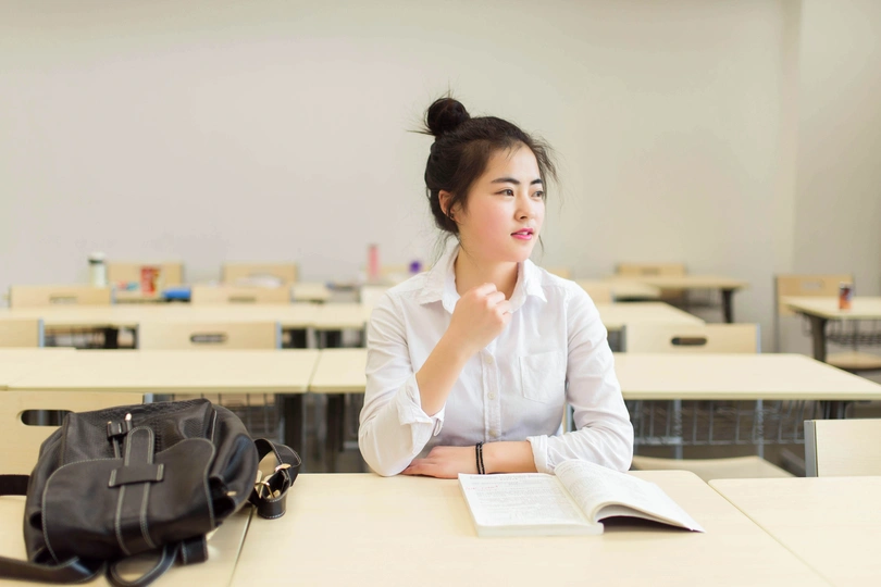 一个年轻女子坐在教室的桌子旁 桌子上有一本书。