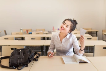 一个年轻女子坐在教室的桌子旁 桌子上堆满了书籍和纸张。