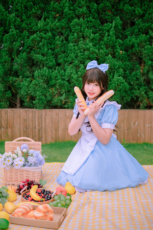 一位穿着蓝色连衣裙的年轻女子手持一个装满面包的篮子 靠近一个水果桌子。