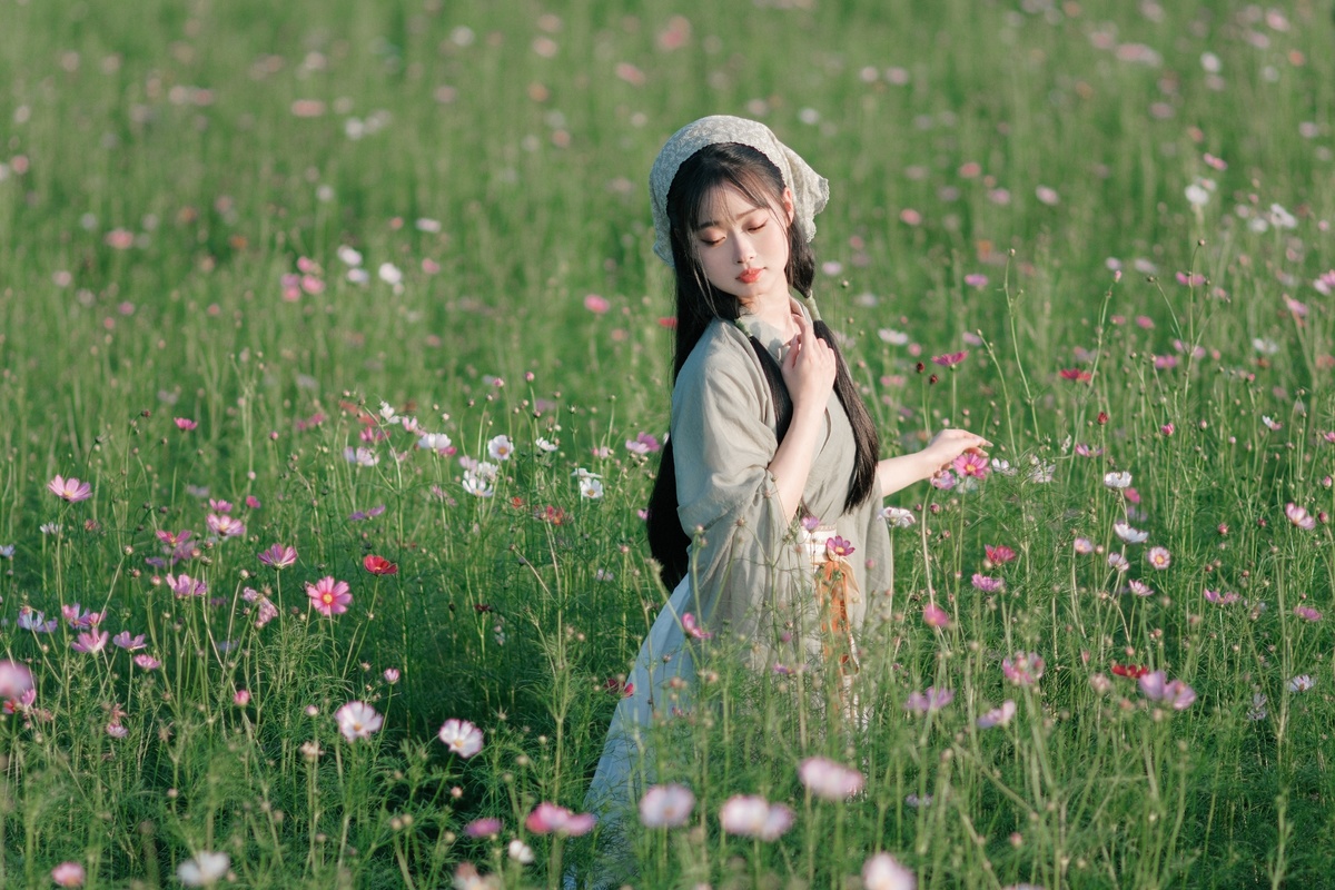 一位年轻女子穿过花田 在草地上采摘花朵。