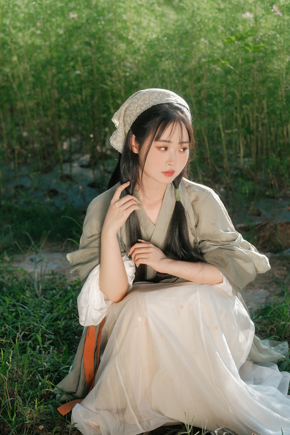 一个穿着白色连衣裙的年轻女子坐在草地上