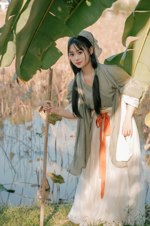 一位穿着白色连衣裙的年轻女子在香蕉树和沼泽地前摆姿势
