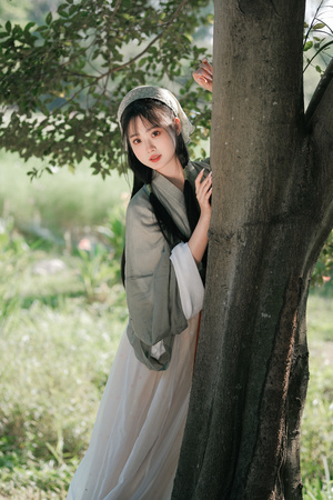 一位年轻女子穿着裙子靠在一棵树上