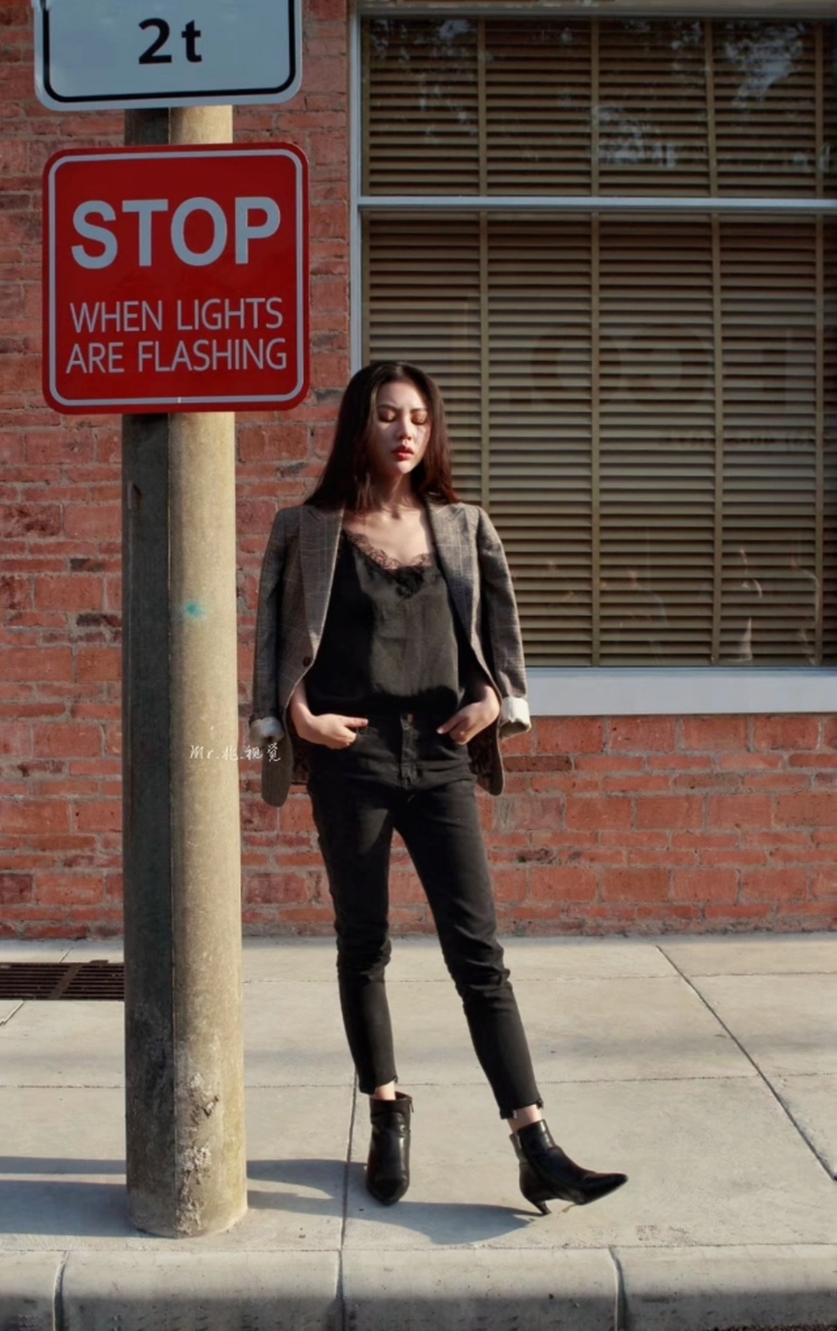 一位女性站在人行道上 靠在一根带有禁止停车标志的柱子上。