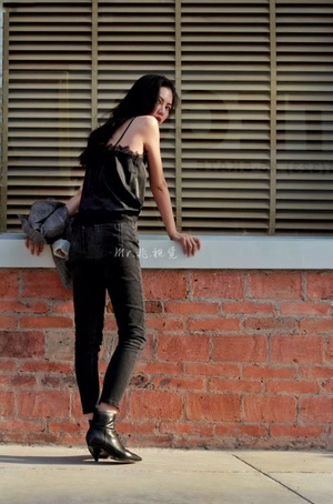 一位穿着黑色牛仔裤的年轻女子站在人行道上 面前有一堵砖墙 靠在一栋建筑上。