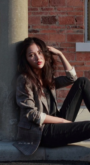 一位年轻的女模特 坐在砖墙边 倚靠在建筑物的墙边